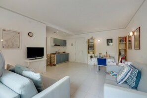 A modern living room with a flat-screen TV, a sofa, a dining table, and a kitchen area in the background.
