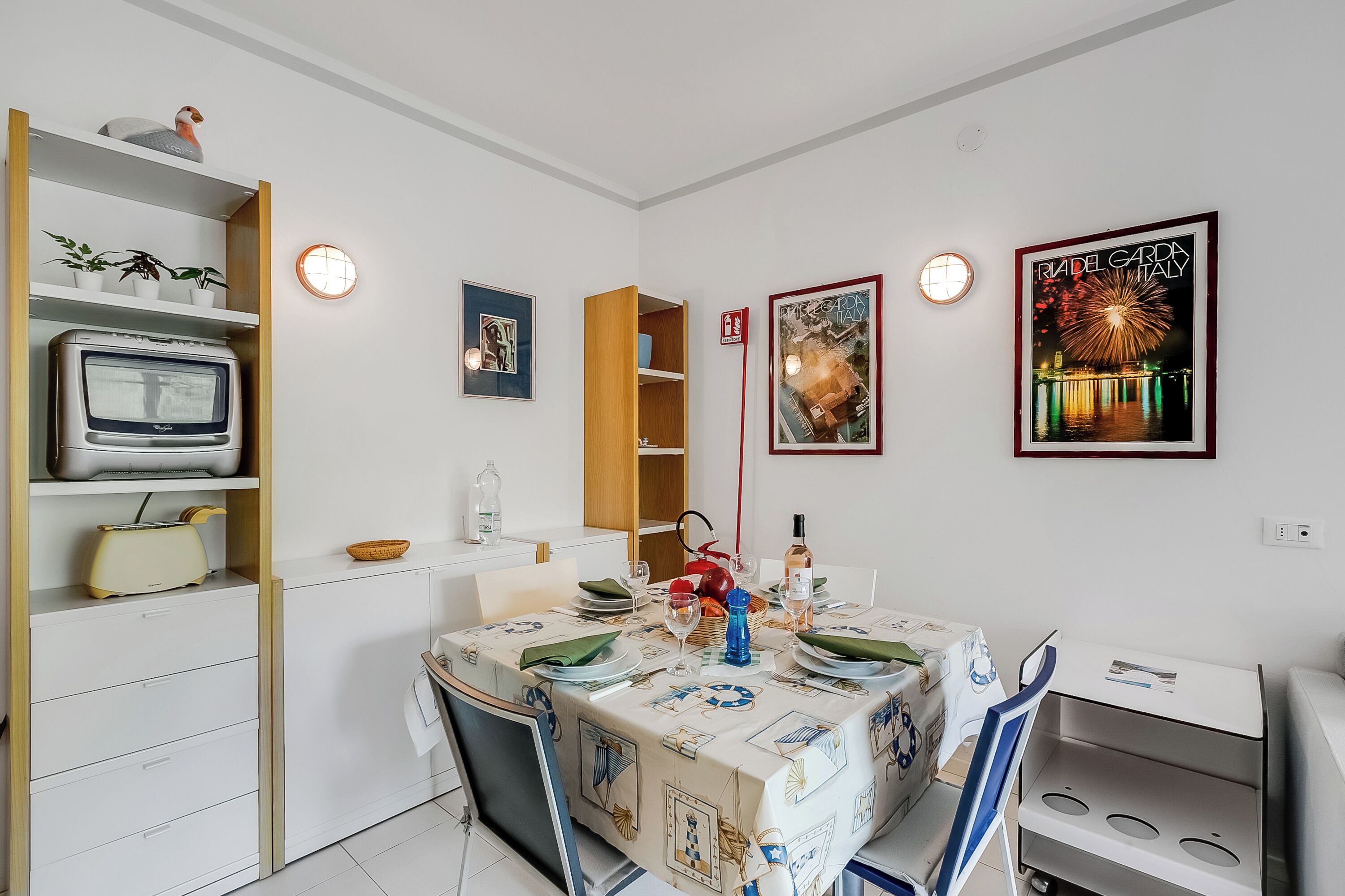 A dining area with a table set for two, a television on a shelf, and various wall decorations including a framed picture of fireworks.