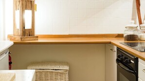 Een keuken met witte kastjes, een houten aanrecht, een fornuis, een rieten mand en een wandlamp.