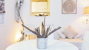 Een witte eettafel met een gevlochten mand met takken, een witte bank met kussens, een wandkast en een decoratief wandobject.