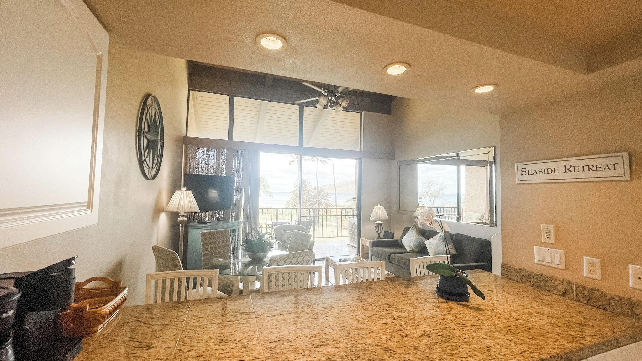 A spacious living area with a large window overlooking the sea, a ceiling fan, and a sign indicating a seaside retreat.
