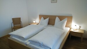 A double bed with white bedding, two bedside tables with lamps, and a wooden chair. - Apartment- 2 persons, 80sqm, 1 bedroom, balcony, WLAN (Schleching)
