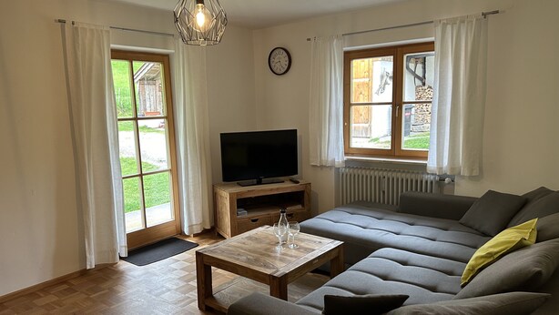 A living room with a sofa, a coffee table, a TV, and a window with curtains. - Apartment- 2 persons, 80sqm, 1 bedroom, balcony, WLAN (Schleching)