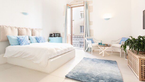Une chambre avec un lit, une petite table, des chaises, une plante en pot et une vue sur le balcon extérieur.