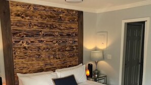 A bedroom with a wooden headboard, a bed with white bedding, a blue throw blanket, a bedside table with a lamp, and a small blue bench.