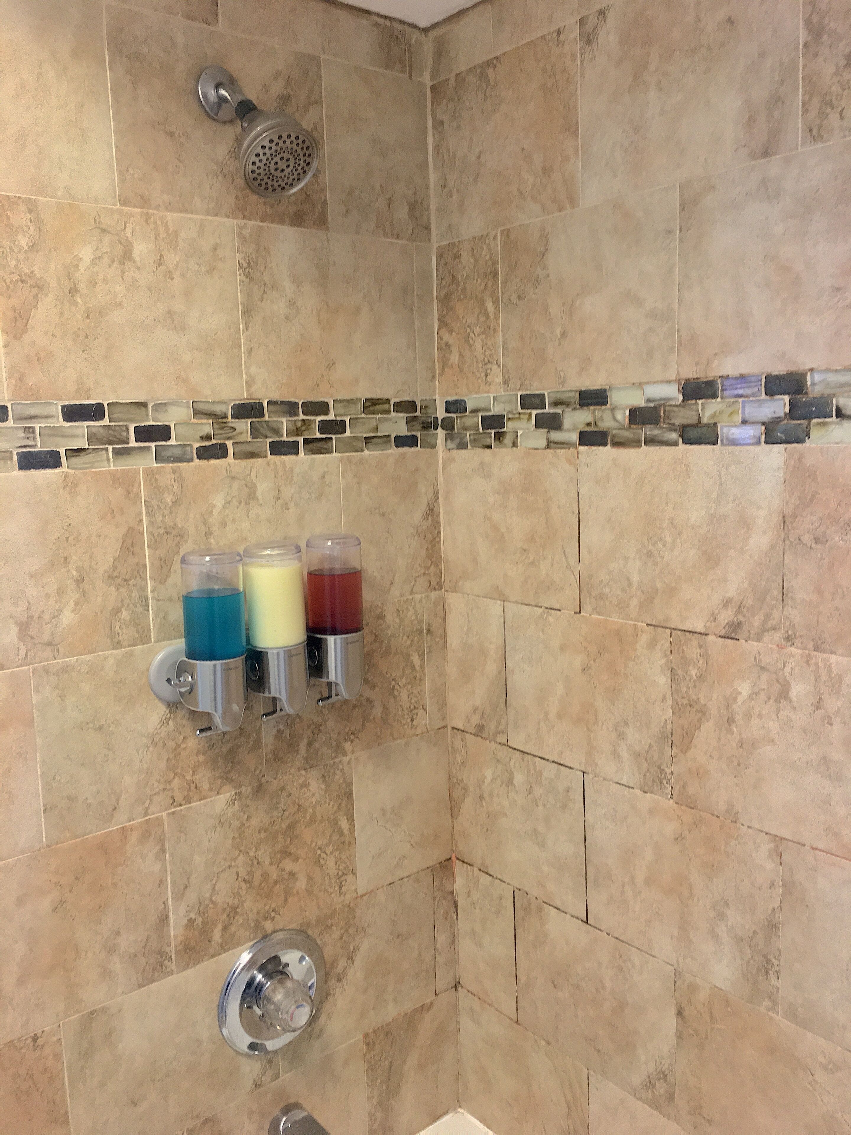 A bathroom with beige tiles, a showerhead, and three soap dispensers.