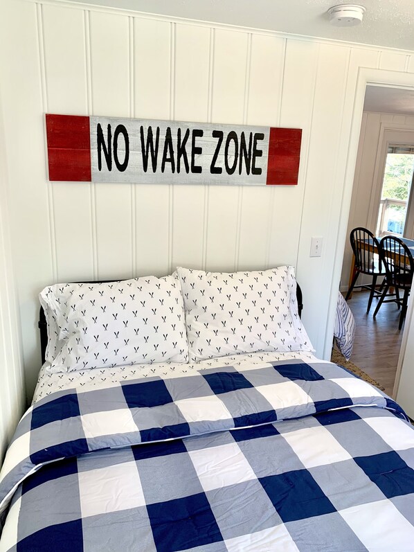 A bedroom with a bed, a 'NO WAKE ZONE' sign, and a checkered bedspread.