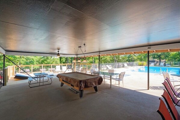 An indoor pool area with a pool table, lounge chairs, and a view of an outdoor pool.