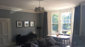 Ein Wohnzimmer mit einem dunkelgrauen Sofa, einem Couchtisch, einem Beistelltisch, einer Lampe und einem Fenster mit Vorhängen.