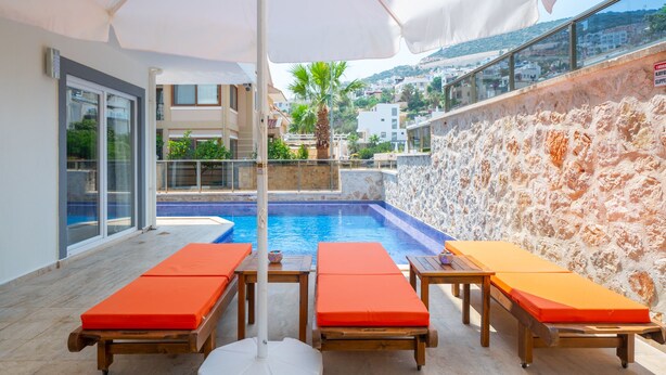 A rooftop pool area with three sun loungers, a table, and a white umbrella.