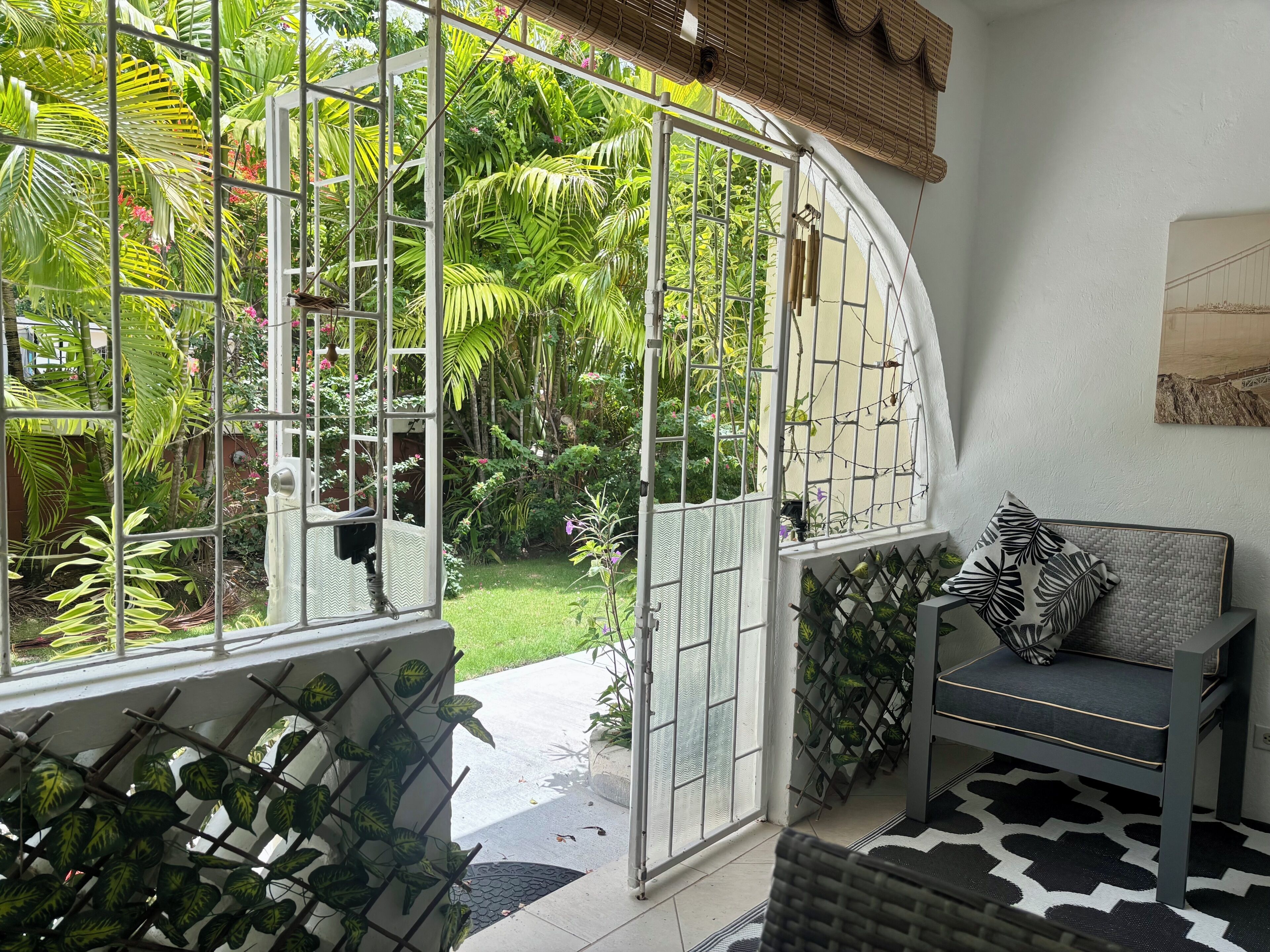 Une pièce donnant sur un jardin luxuriant grâce à une porte vitrée, un canapé gris agrémenté d’un coussin à motifs et un tapis noir et blanc.