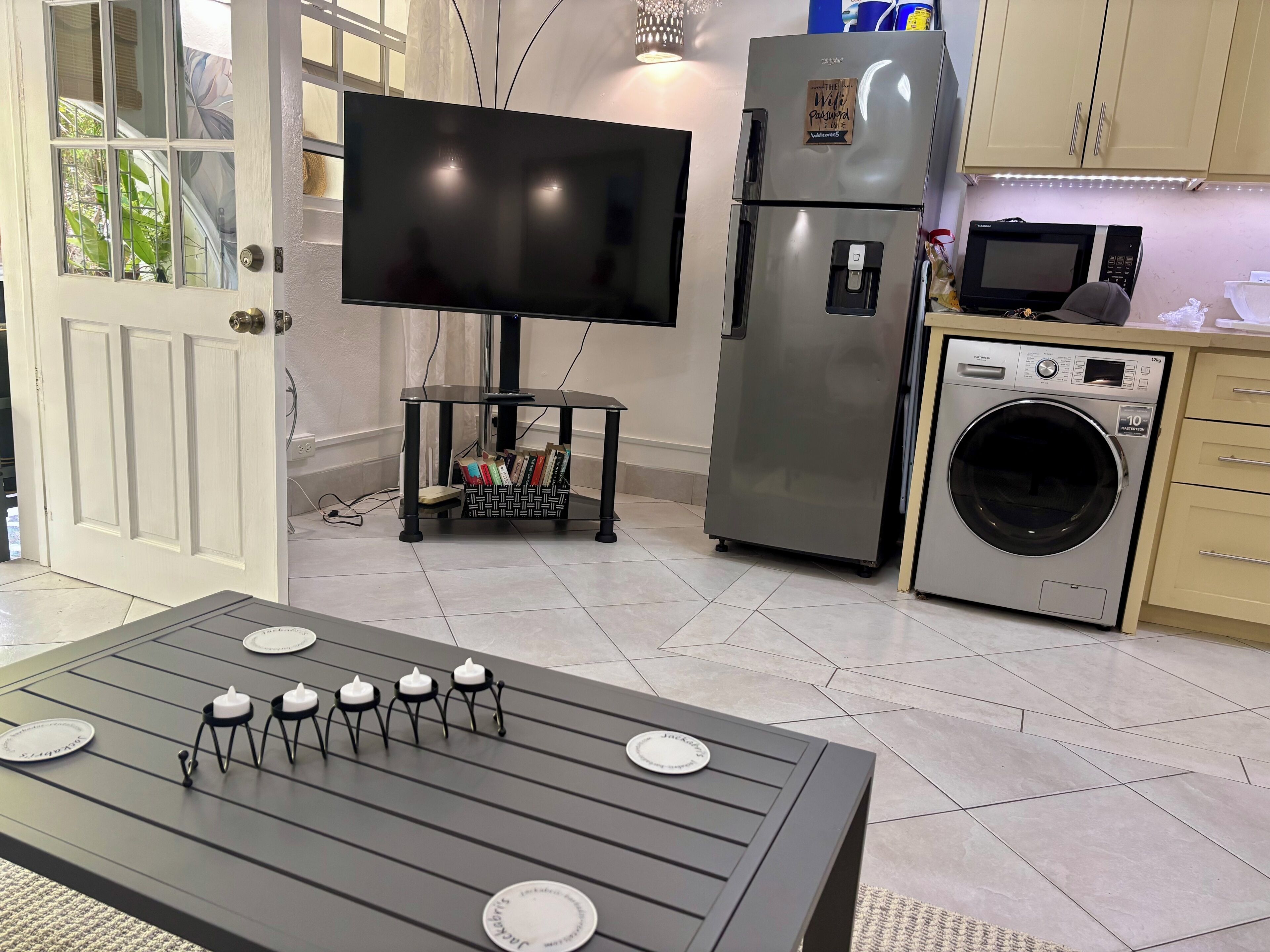 Une cuisine moderne équipée d’un téléviseur à écran plat, d’appareils électroménagers en acier inoxydable et d’un coin repas avec une table dressée pour quatre personnes.