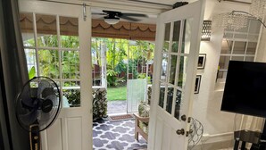 Une pièce dotée d’un grand ventilateur, d’une télévision et d’une porte donnant sur un jardin.
