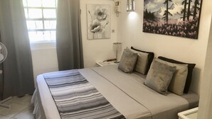 Une chambre à coucher comprenant un lit, des rideaux, un climatiseur fixé au mur, une lampe fixée au mur et un tableau.
