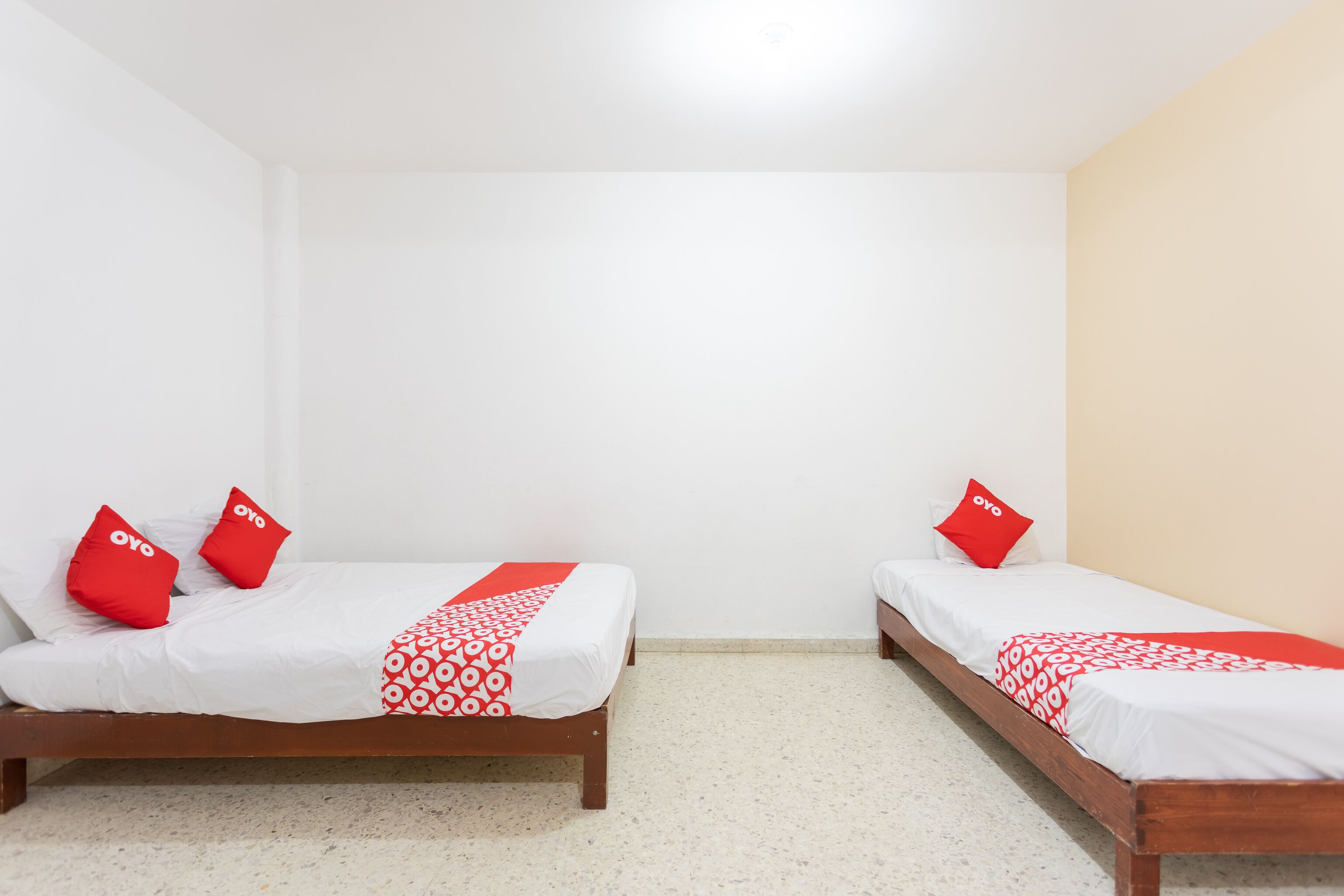 Two single beds with red pillows and white bedding in a room with plain walls and a tiled floor.