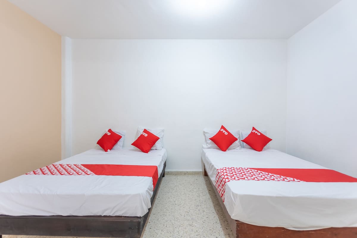 A room with two single beds, each with a red and white bedspread and matching pillows. The room has white walls and a tiled floor.