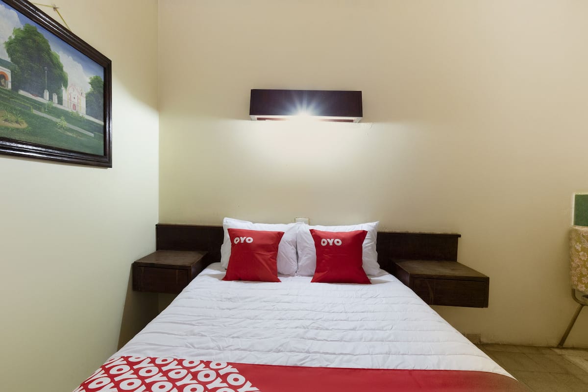 A hotel room with a bed, two nightstands, a painting on the wall, and a red and white patterned bedspread.