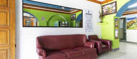 A lobby with a red leather sofa, a large mirror, and a green wall with a poster.