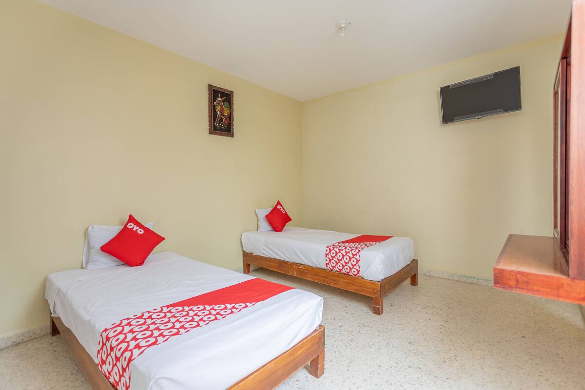 Two single beds with red and white bedding, a small wall-mounted TV, and a framed picture on the wall.