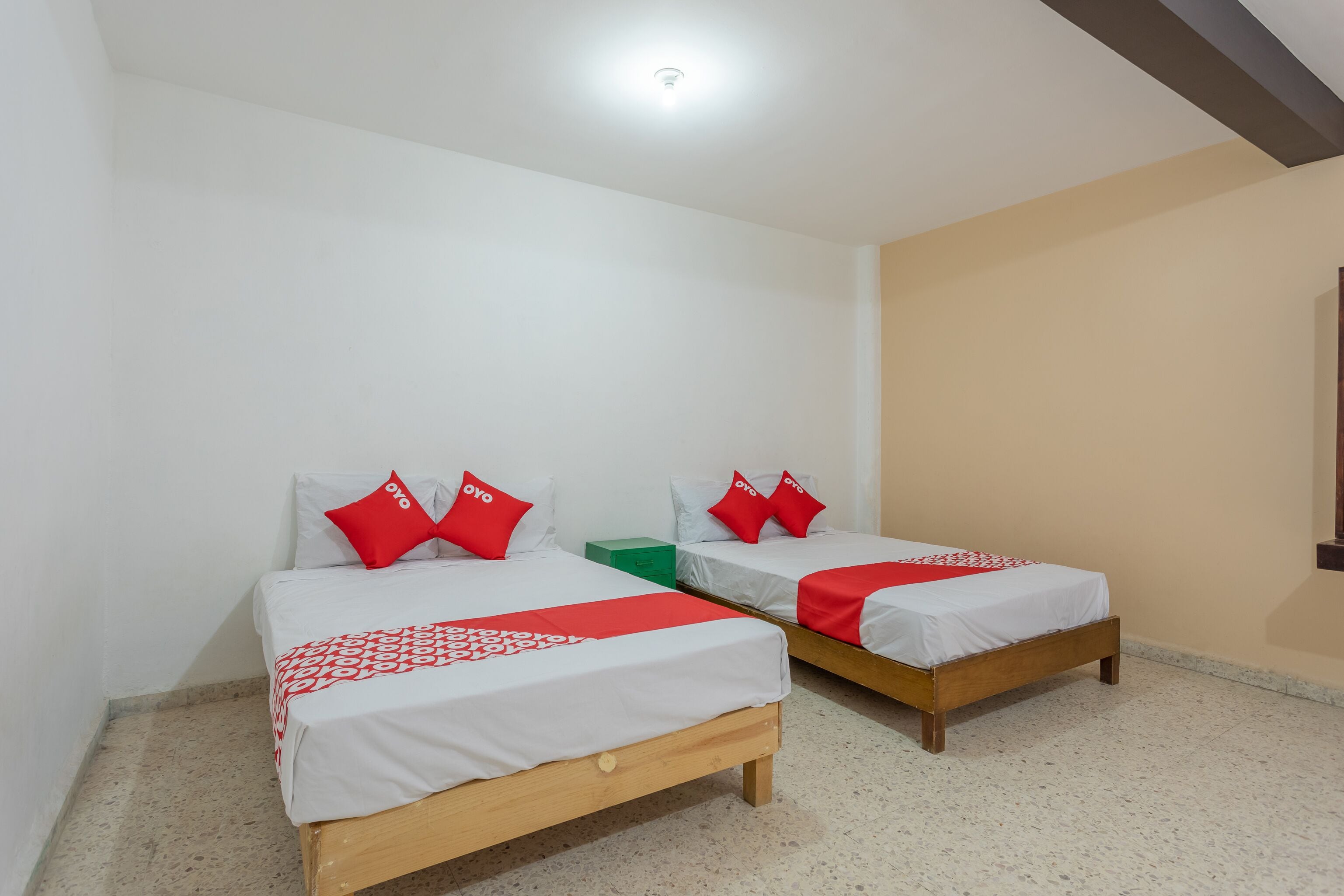 Een kamer met twee bedden, elk voorzien van witte beddengoed en rode accenten, een groene nachtkastje en een plafondlamp.