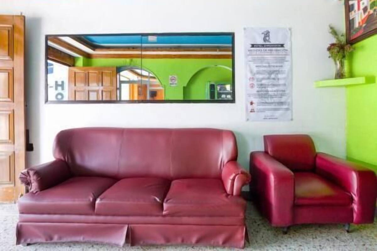 A red leather sofa and armchair in a room with a green wall, wooden ceiling, and a framed picture on the wall.