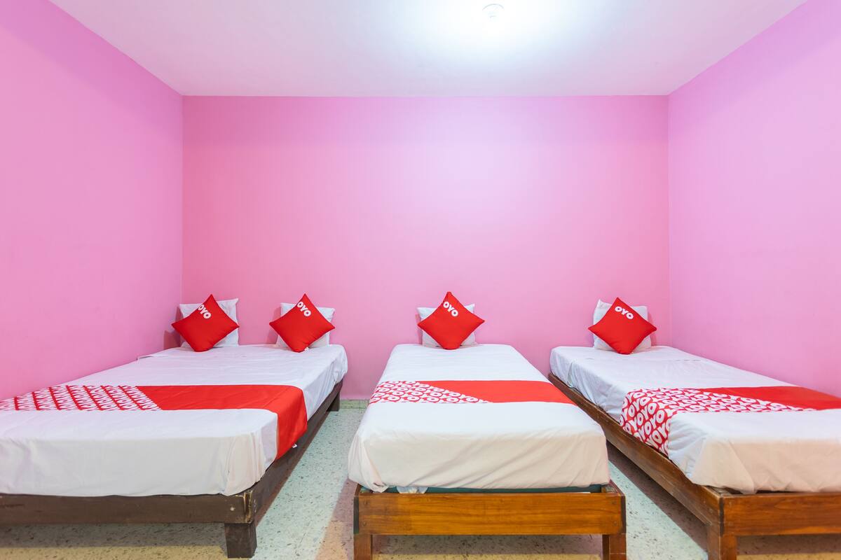 A room with three beds, each with a red and white bedspread and matching pillows.