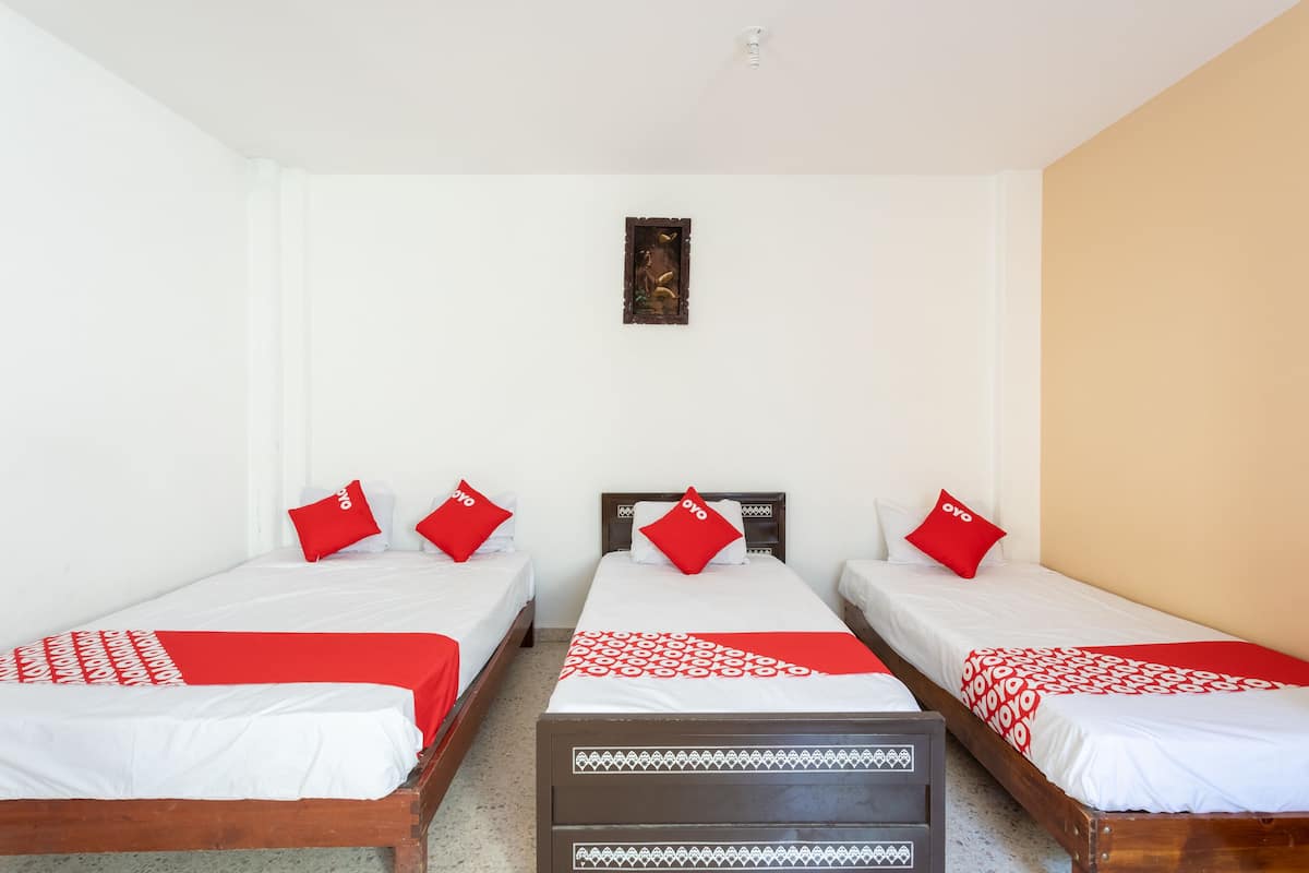 A hotel room with three single beds, each with a red and white bedspread and matching pillows.
