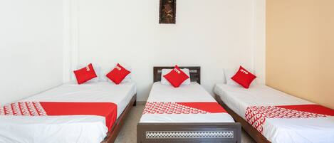 Una habitación de hotel con tres camas individuales, cada una con una colcha y almohadas rojas y blancas.