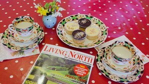 A table with a polka dot tablecloth, a magazine titled 'Living North', and a plate with cupcakes and a teapot.