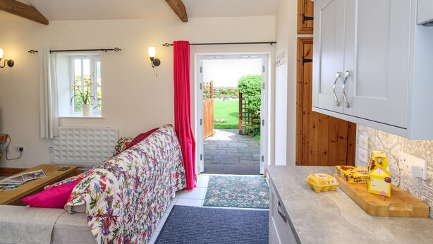 A cozy room with a bed, a small table, a window with curtains, a door leading outside, and a kitchen area with cabinets and a countertop.