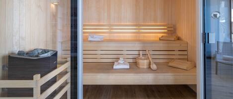 A wooden sauna with benches, a bench with towels, and a wooden bucket.