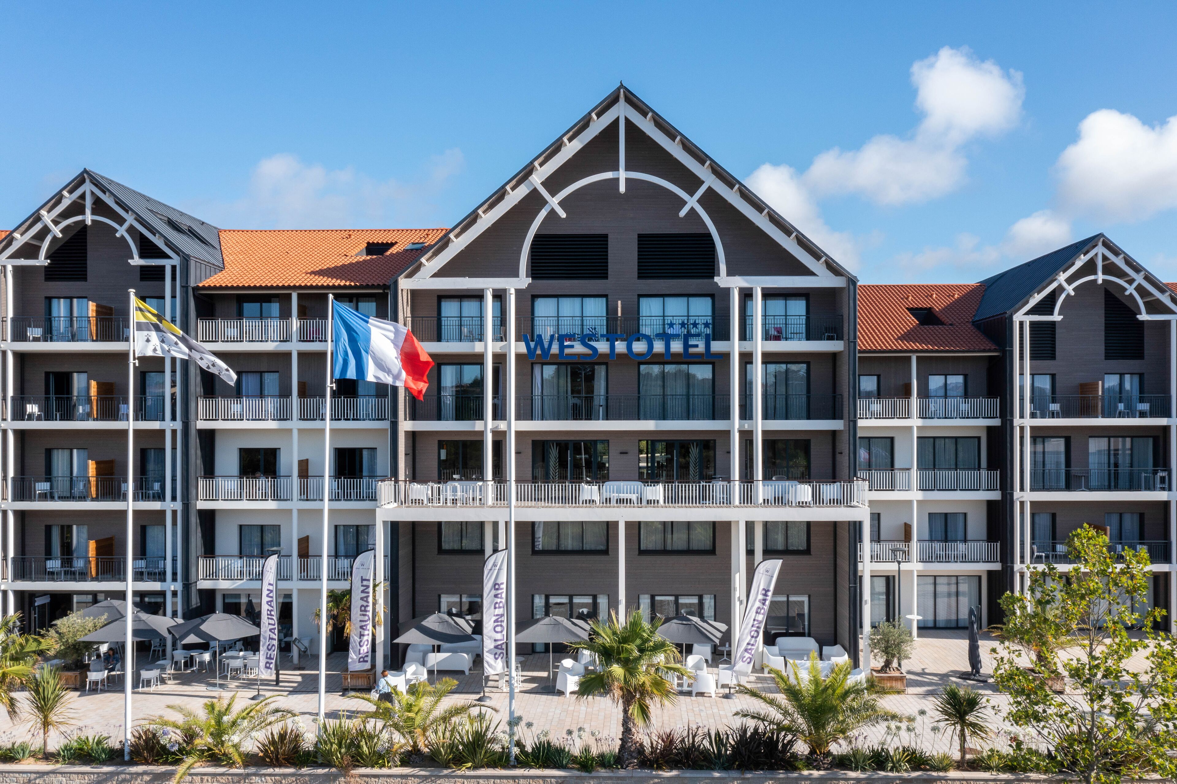 Un hôtel à plusieurs étages doté de balcons, d’un espace extérieur aménagé et de drapeaux.