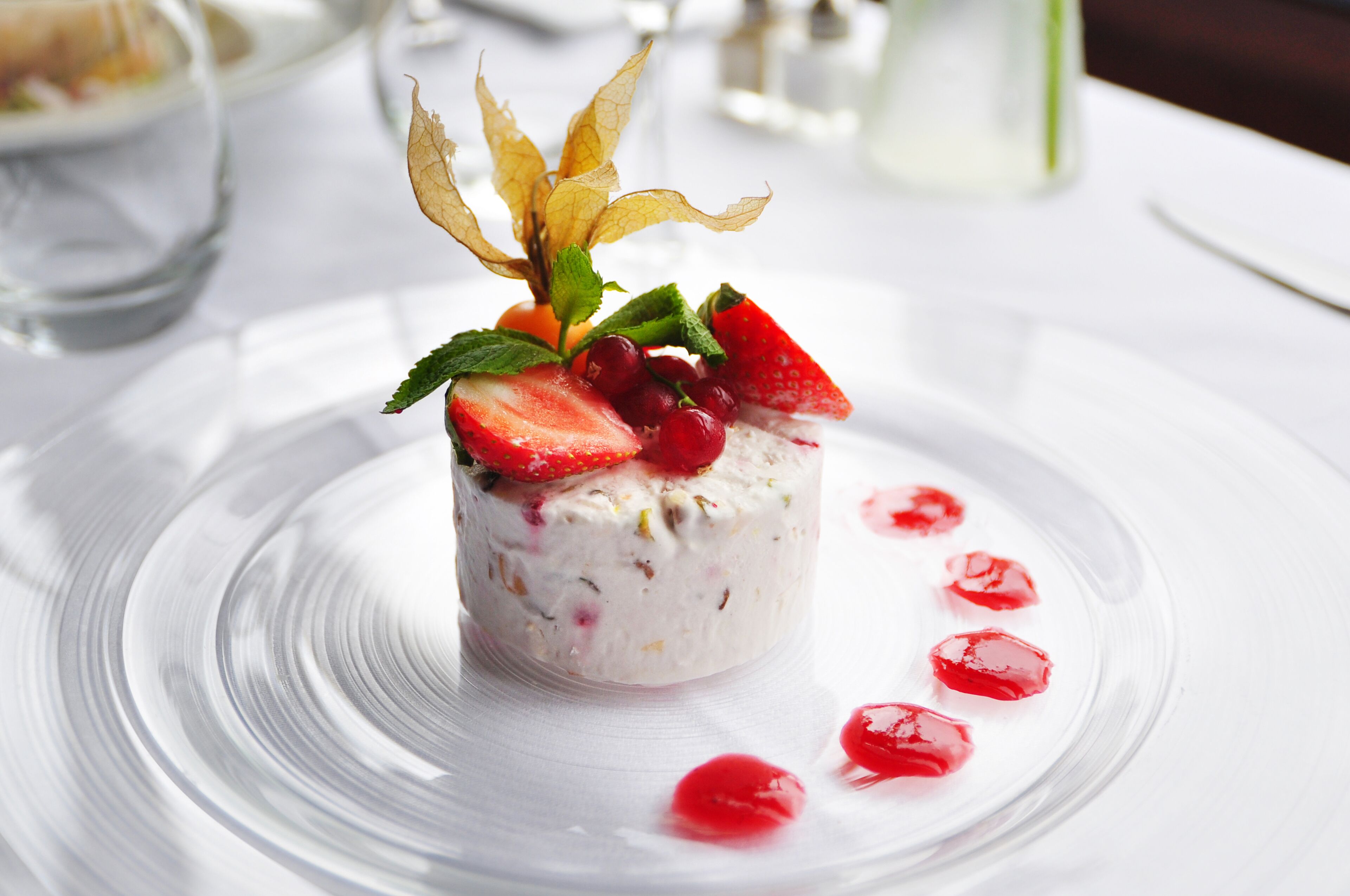 A dessert with strawberries and red berries on a clear glass plate.