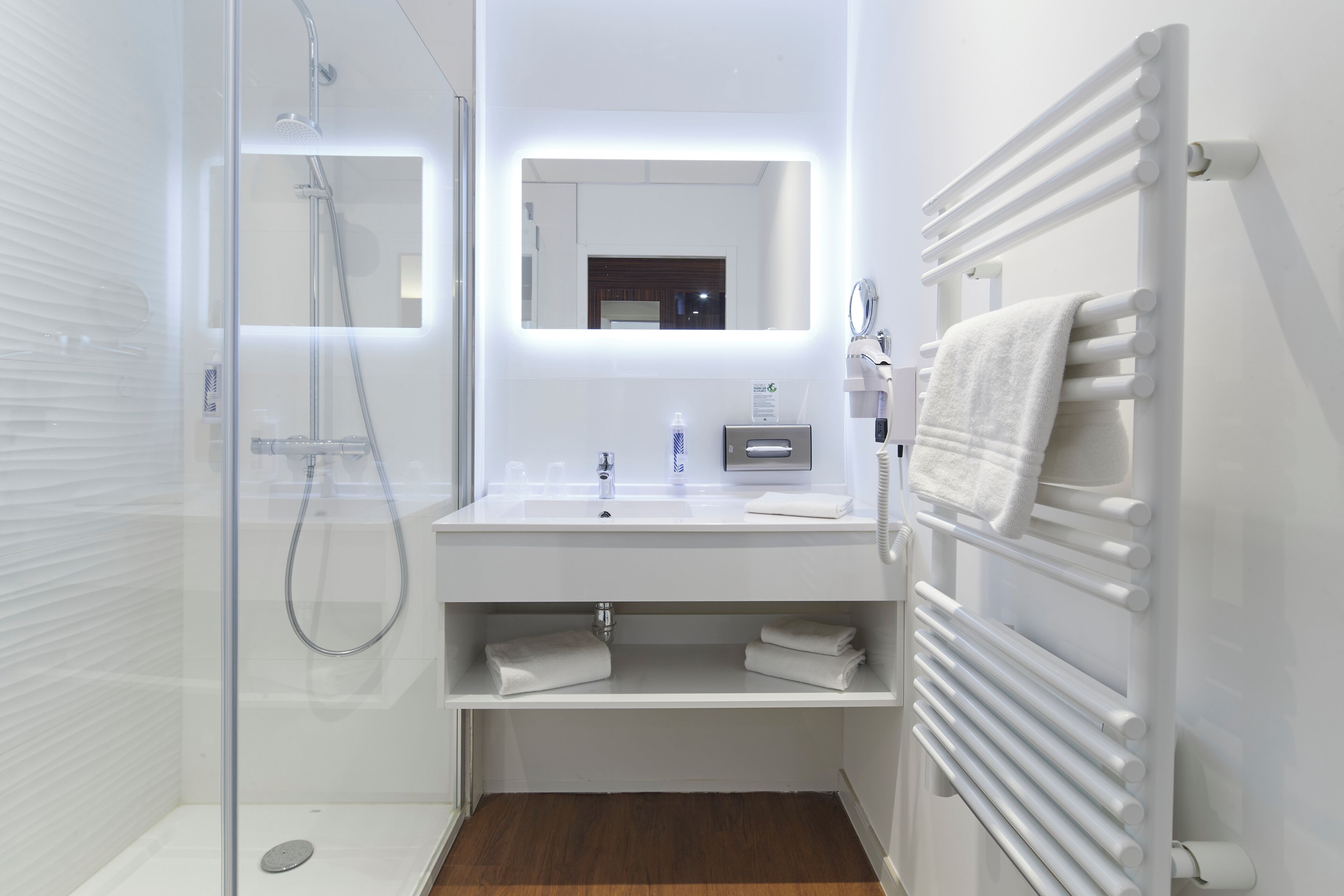 Une salle de bain moderne avec une douche à parois de verre, un lavabo blanc avec un miroir au-dessus, et un porte-serviettes sur lequel est posée une serviette.