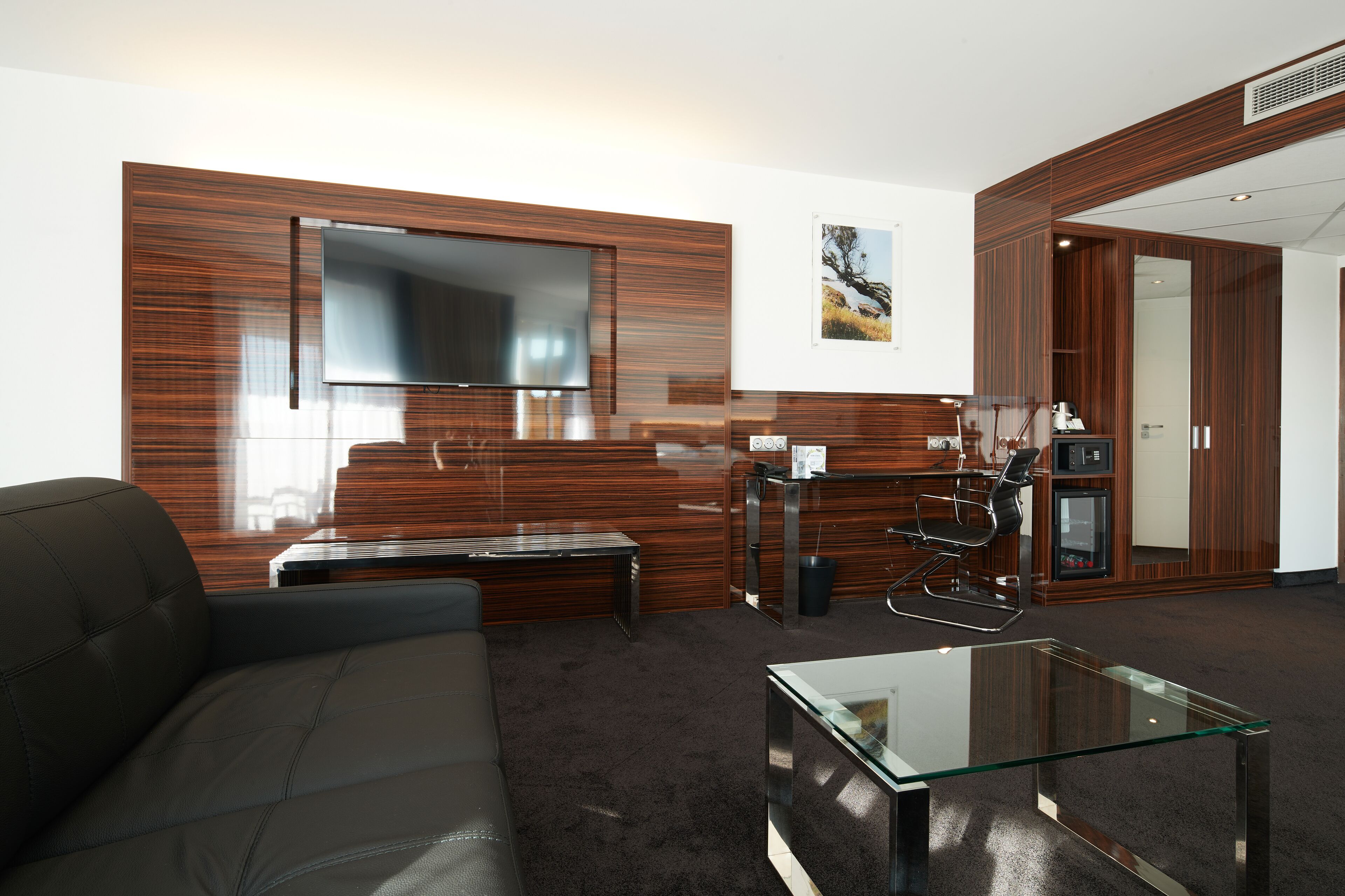 Een moderne woonkamer met een leren bank, een glazen salontafel en een flatscreen televisie bevestigd aan een houten wand.
