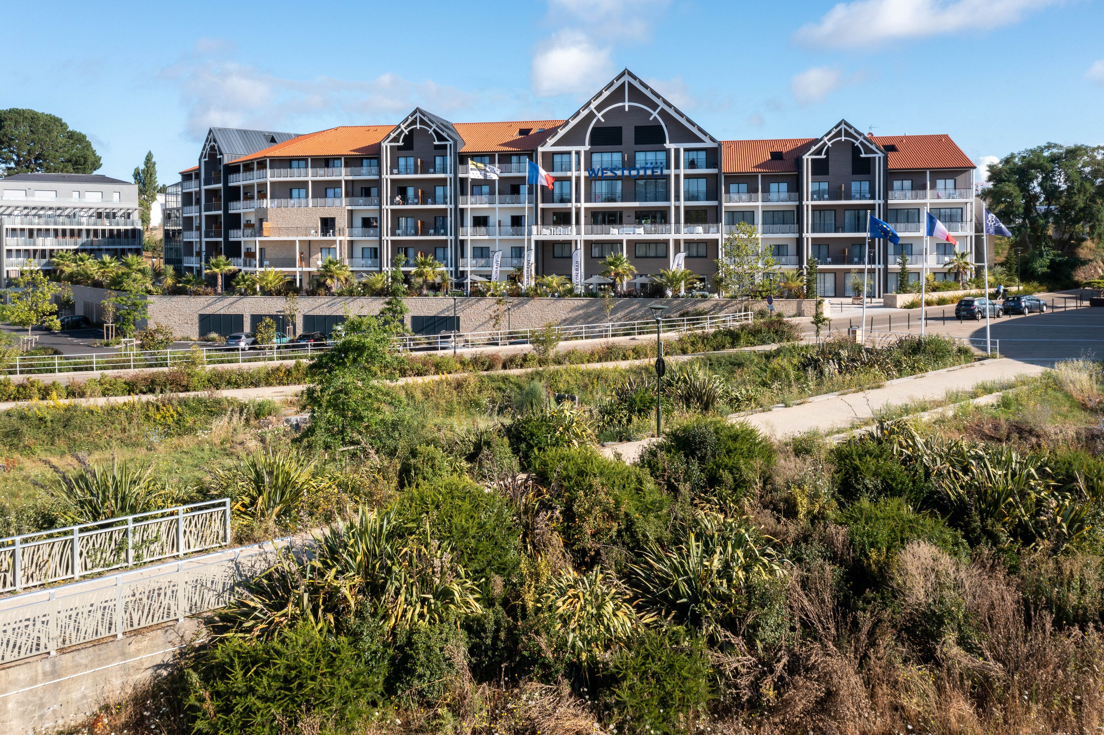 A multi-story hotel with balconies, a parking area, and a landscaped garden.