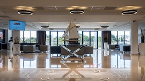A modern lobby with a sailboat sculpture, large windows, and a digital screen displaying room information. - Westotel Pornic (Pornic)