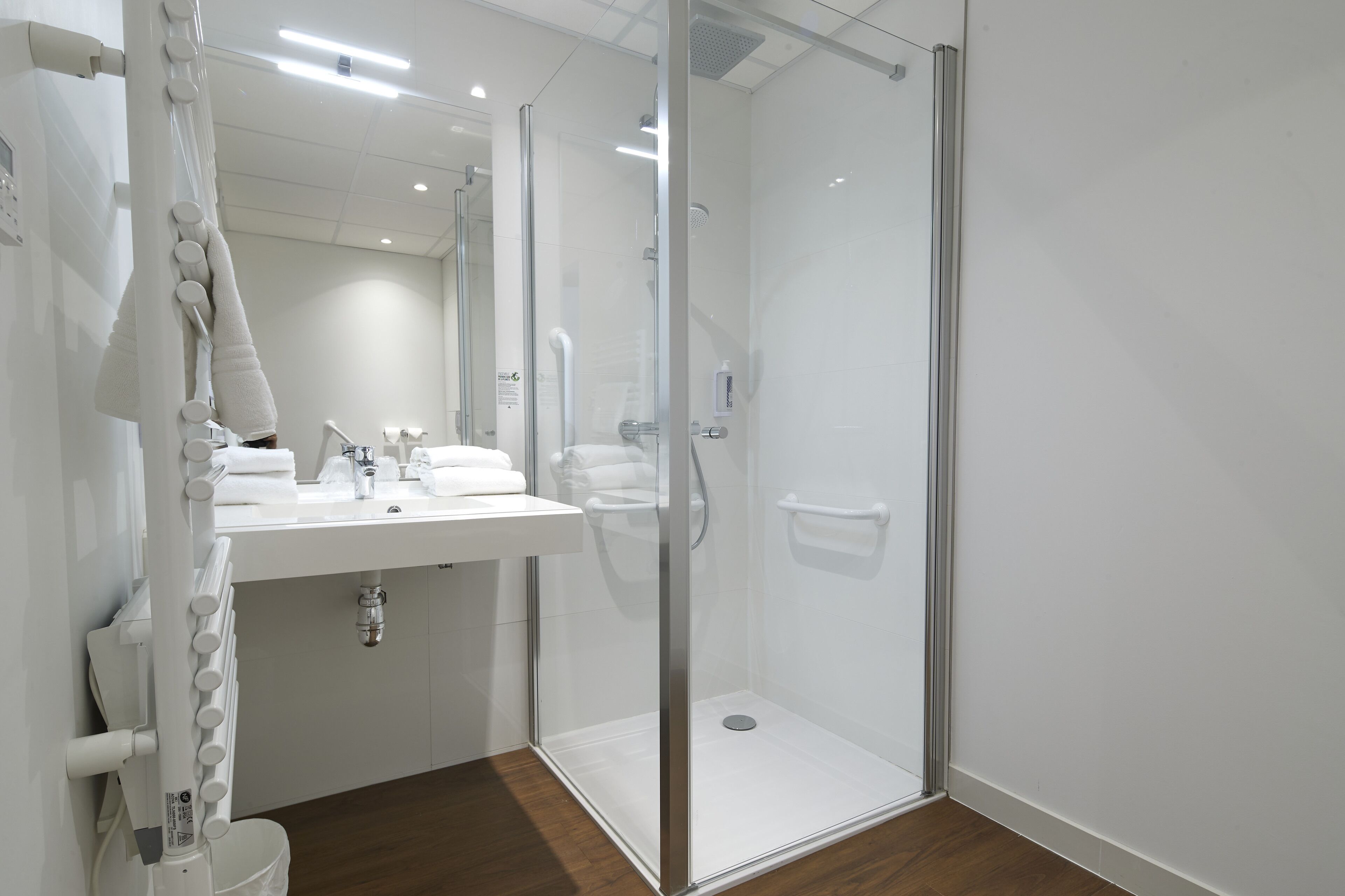 Un baño moderno con cabina de ducha de vidrio, lavamanos blanco y espejo.