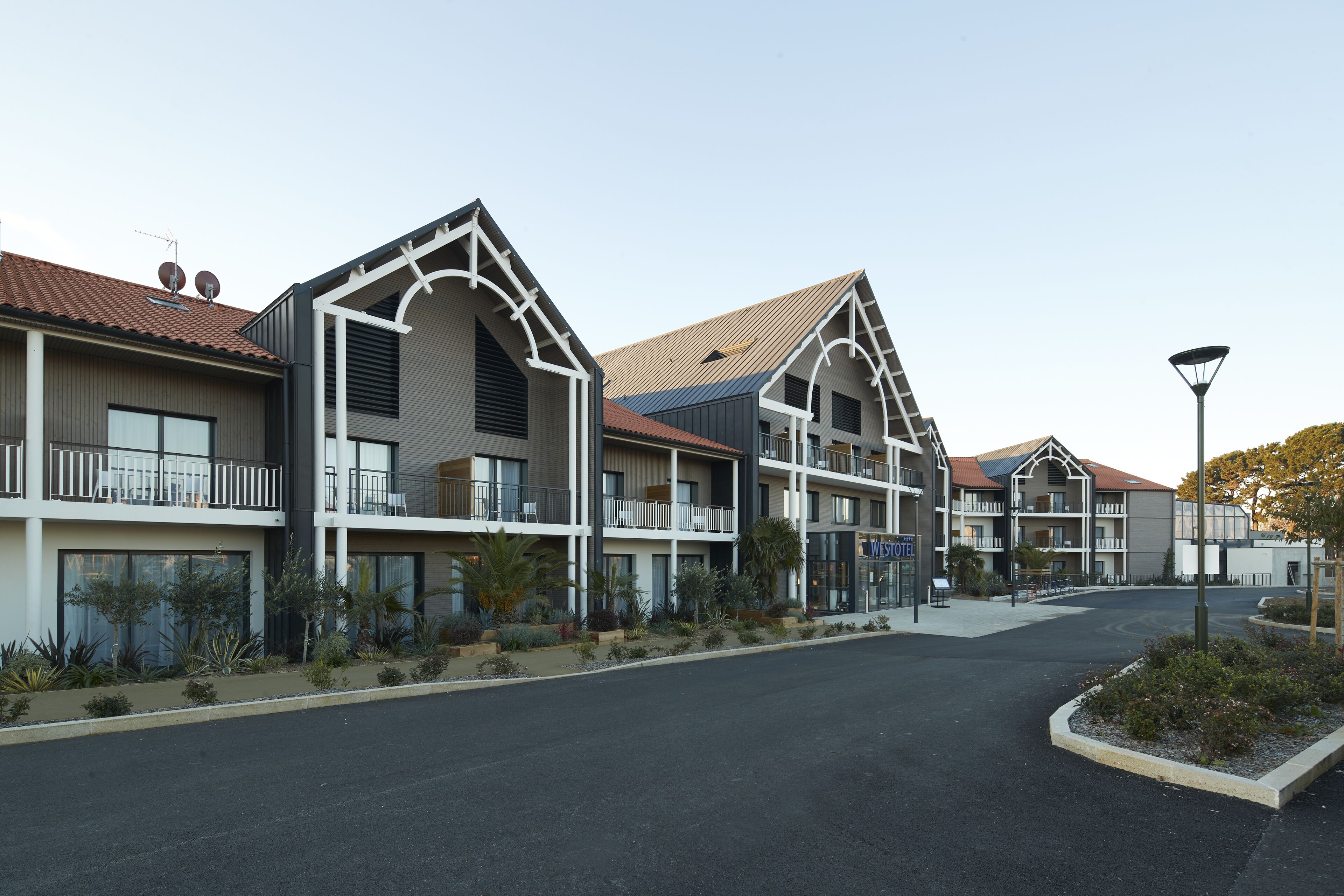 A modern hotel with multiple balconies, a central courtyard, and a parking area.