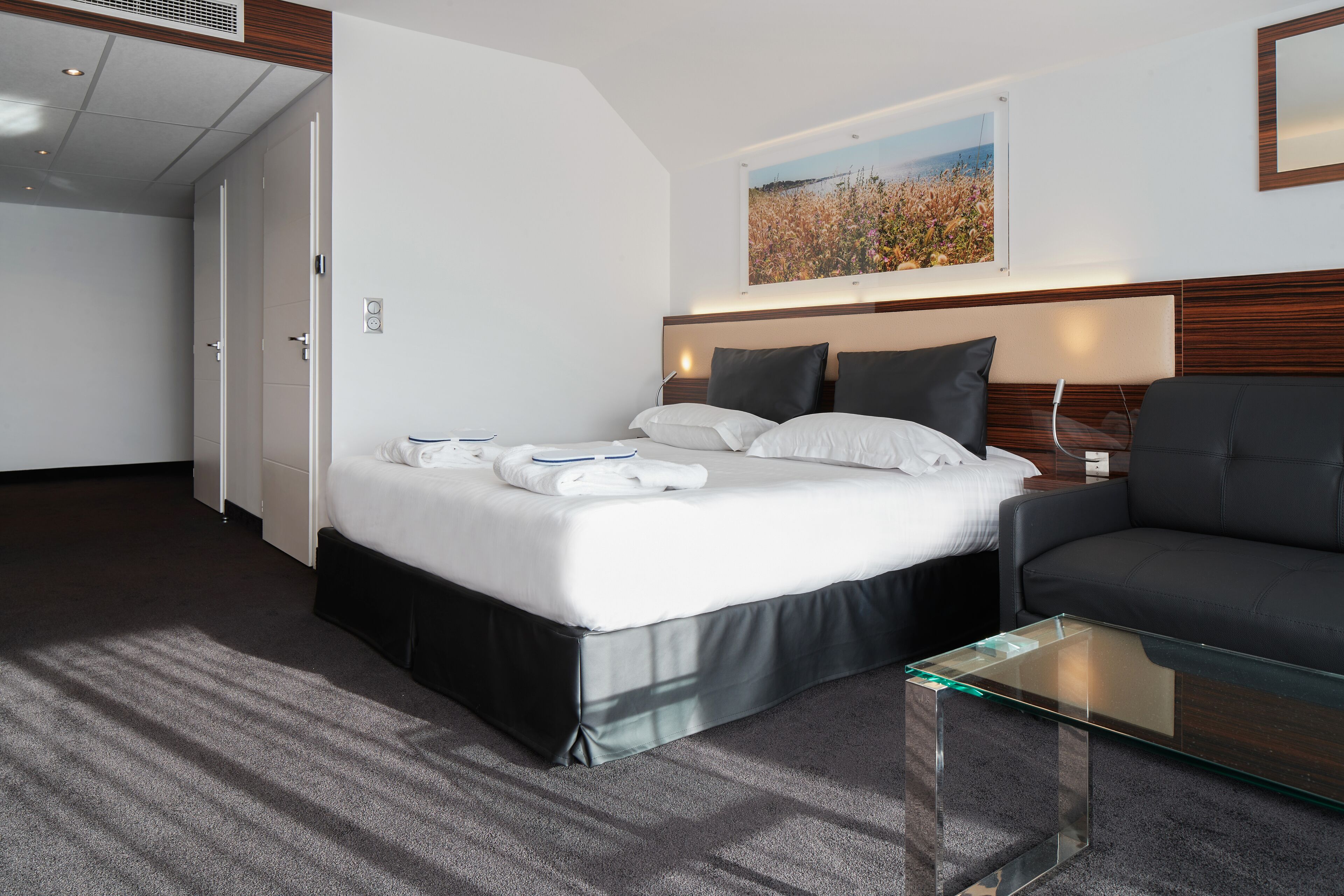 A hotel room with a bed, a glass coffee table, a sofa, and a painting on the wall.
