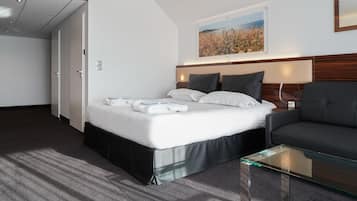 A hotel room with a bed, a glass coffee table, a sofa, and a painting on the wall.