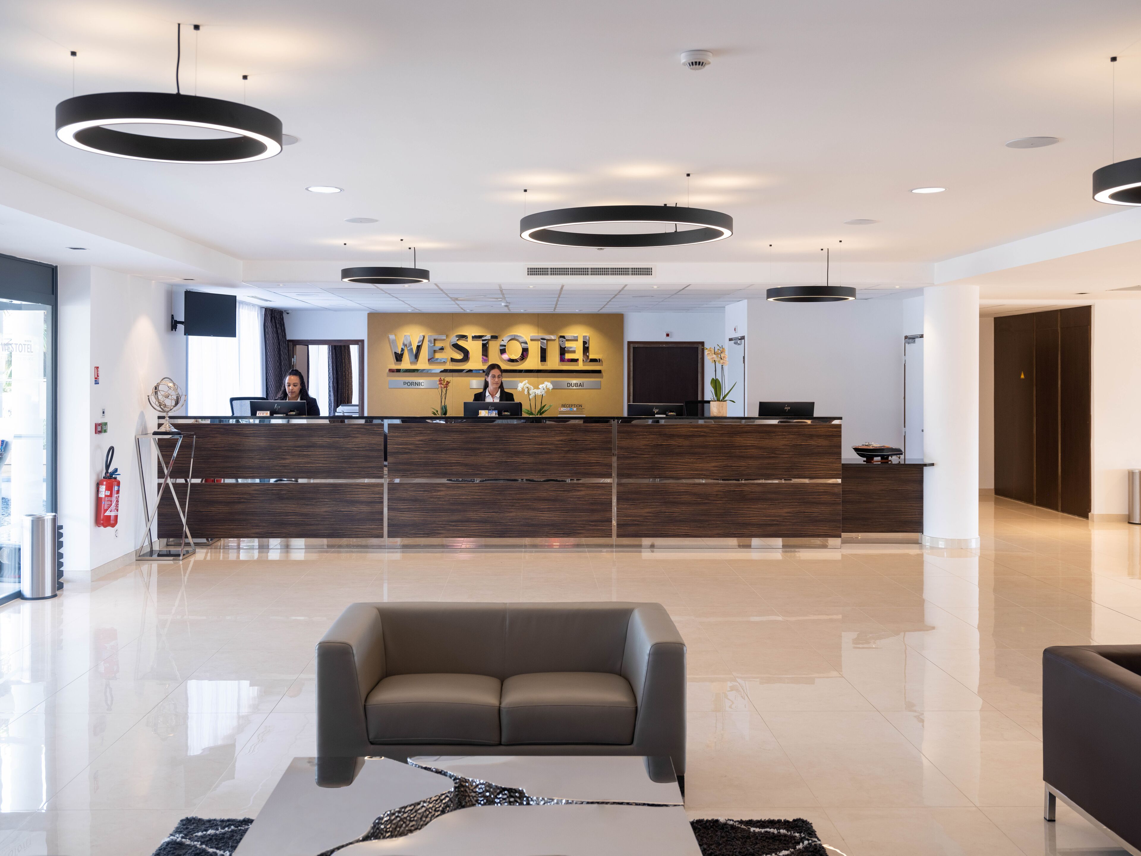 Un hall d’hôtel moderne avec un comptoir d’accueil, des fauteuils en cuir et un sol propre et bien entretenu.