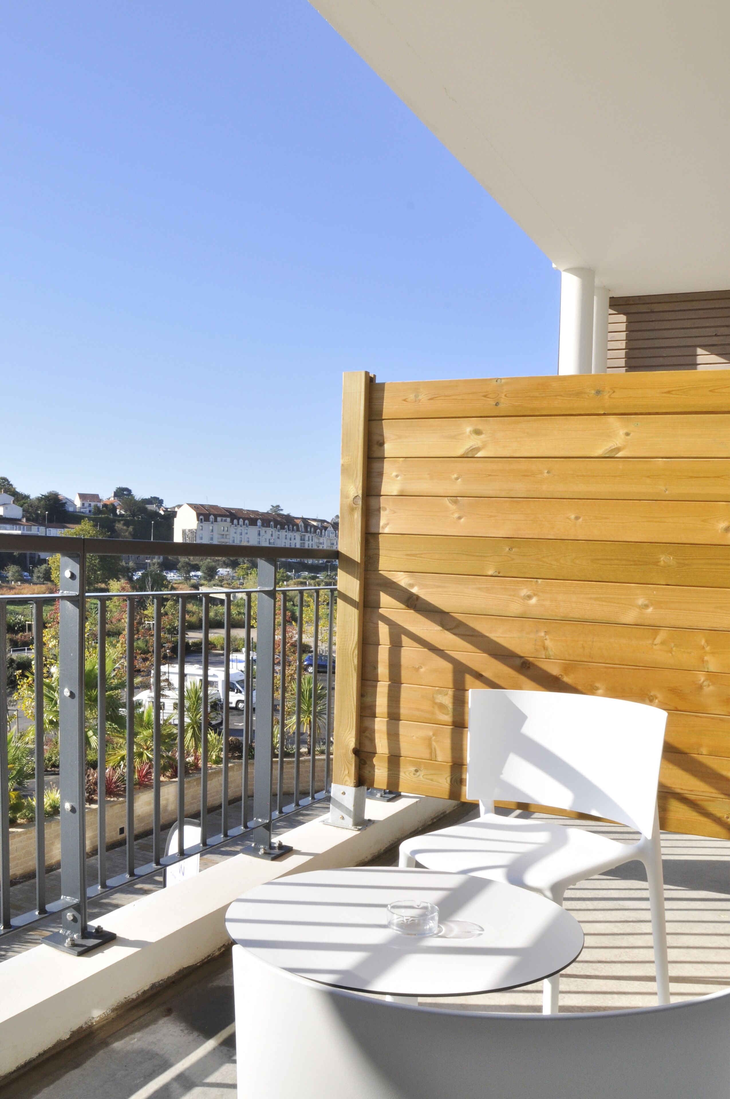 A balcony with a wooden fence, white chairs, and a table.