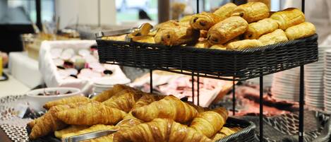 Une variété de pâtisseries, dont des croissants et d’autres viennoiseries, présentées sur des présentoirs en osier.