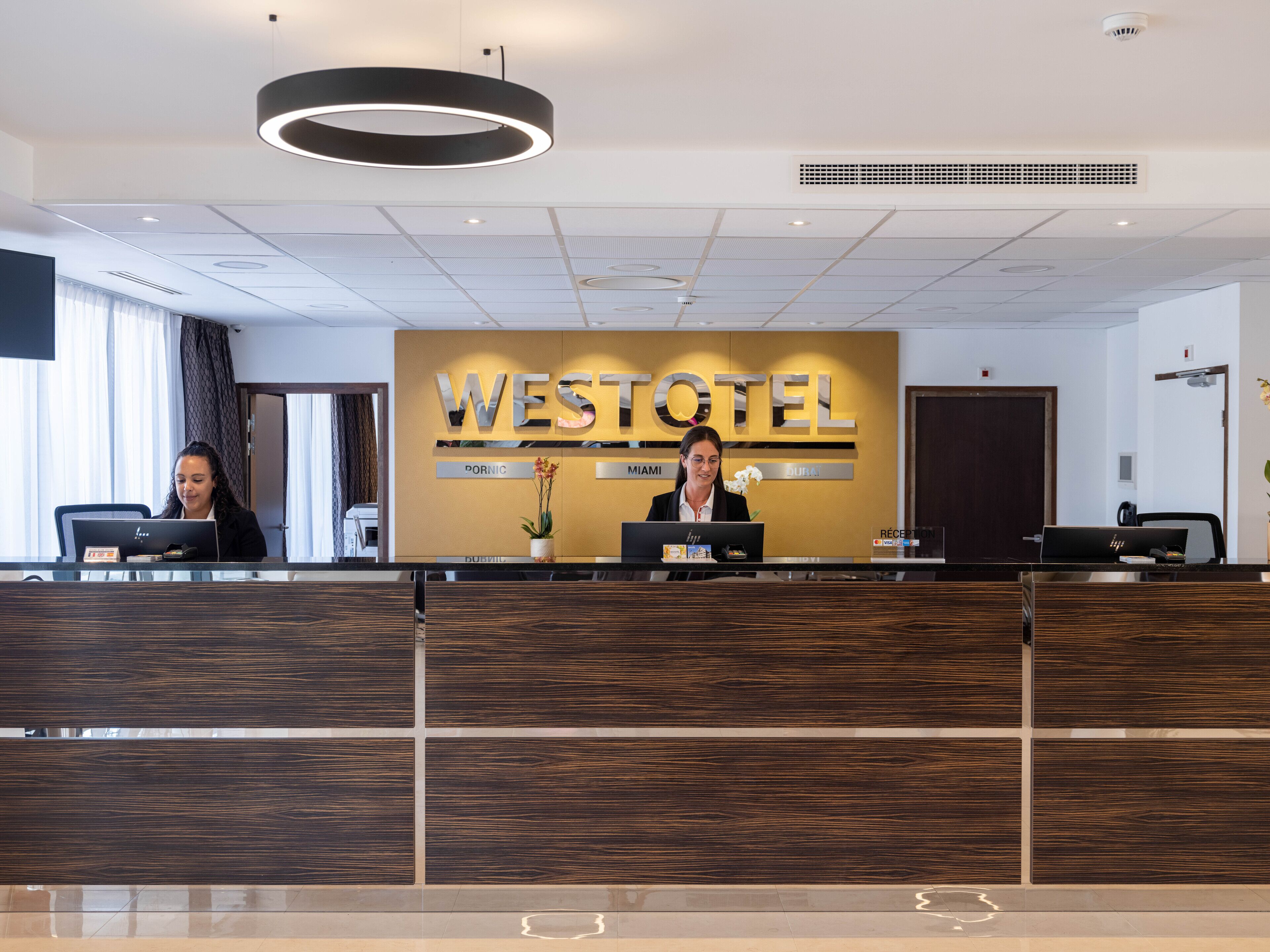 A reception desk at the Westotel with two receptionists, a modern design, and a large sign.