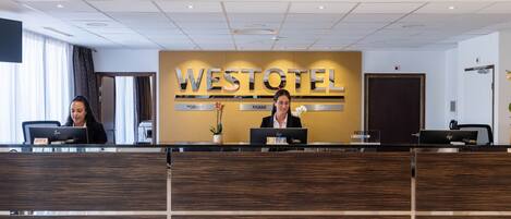 A reception desk at the Westotel with two receptionists, a modern design, and a large sign.