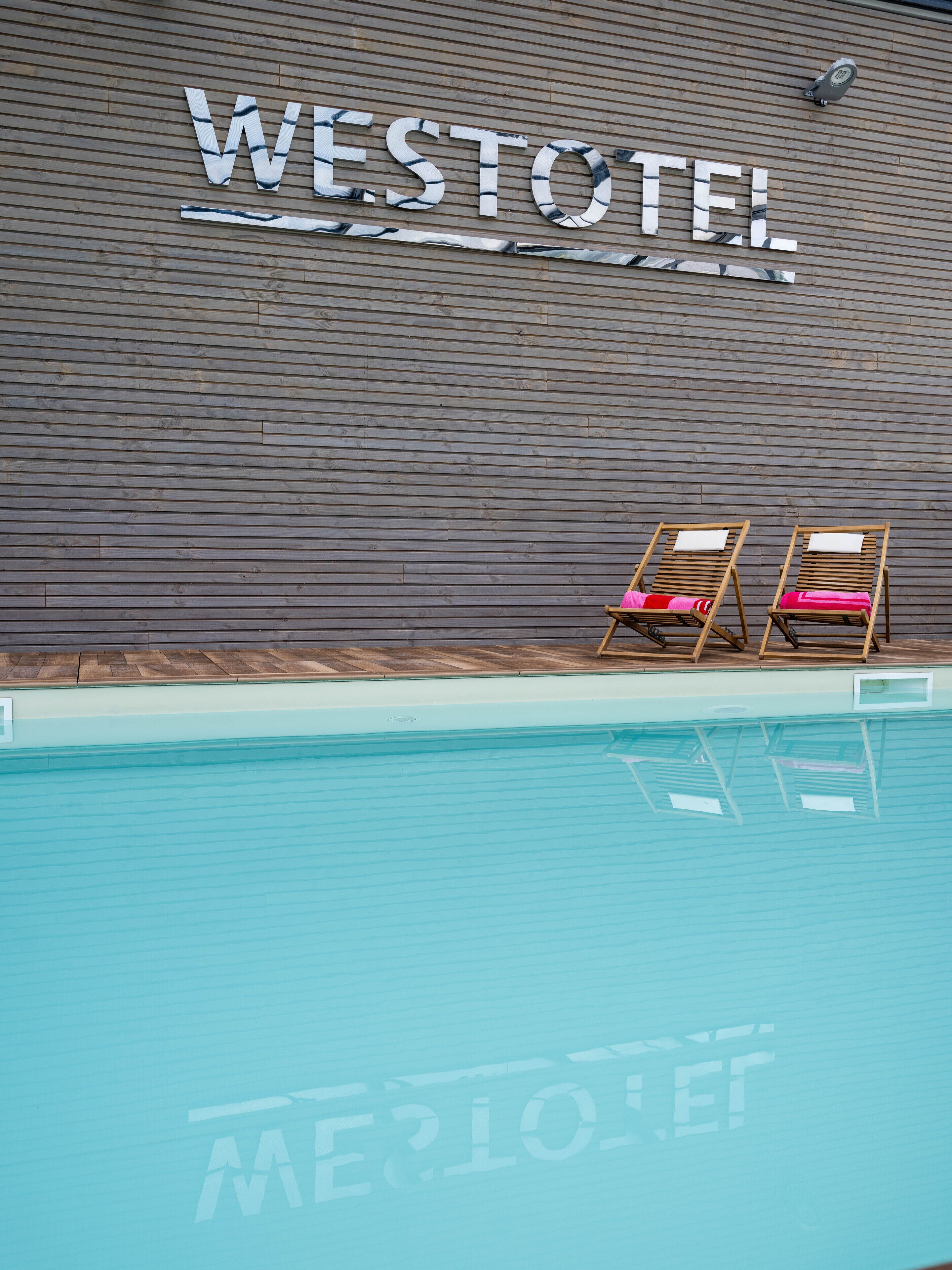 A Westotel sign on a wooden wall above a swimming pool with two lounge chairs.
