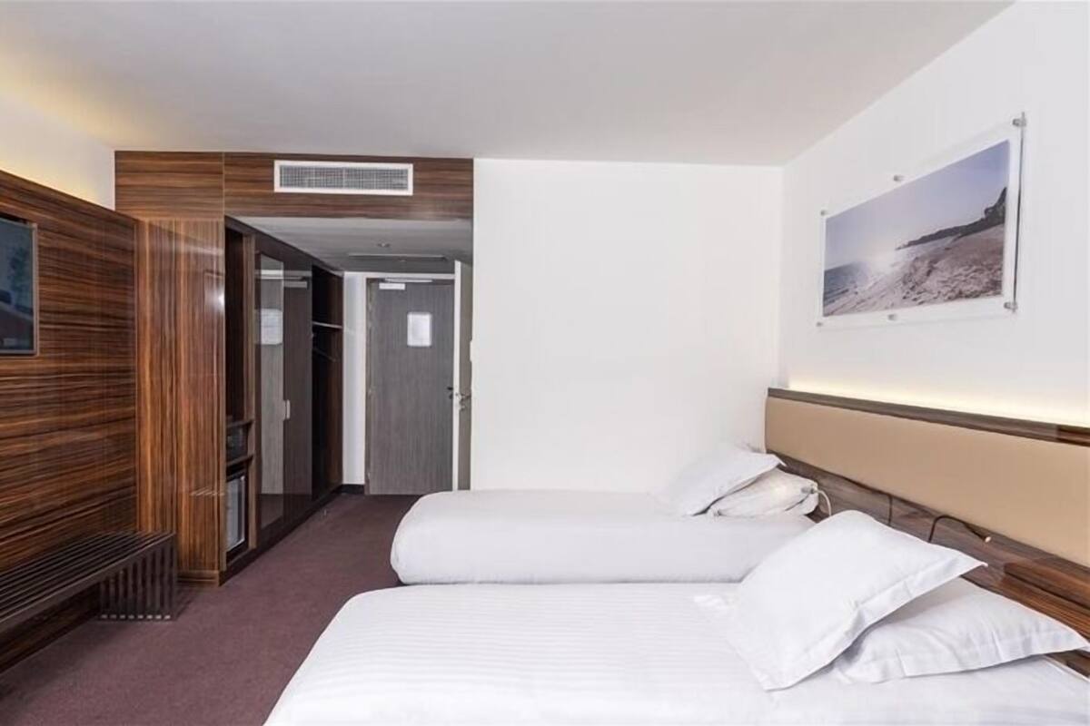 A hotel room with a bed, a bench, a wardrobe, and a painting on the wall.