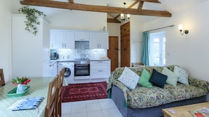 A cozy living room with a sofa, a dining table with a polka dot tablecloth, and a kitchen area with white cabinets and a washing machine. -  YORK single storey cottage ,gardens & open views.Thicket Priory & Derwent Ings. (Thorganby, York)