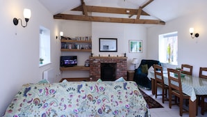 A cozy living room with a fireplace, wooden beams, a bookshelf, and a dining area with chairs and a table. -  YORK single storey cottage ,gardens & open views.Thicket Priory & Derwent Ings. (Thorganby, York)